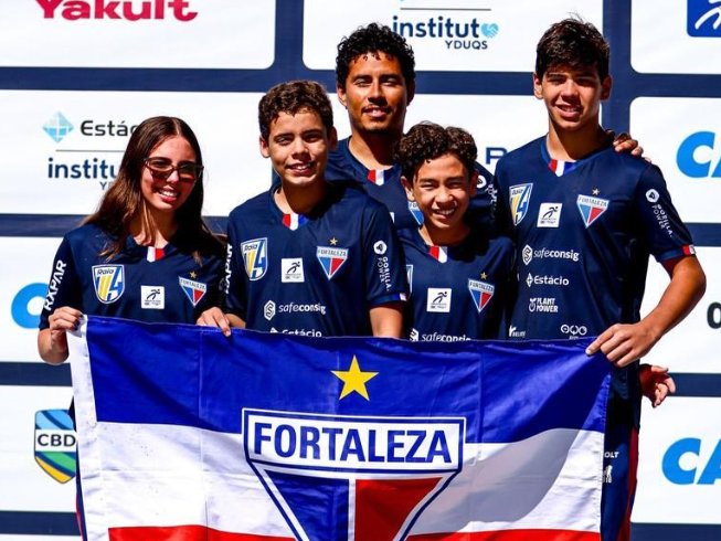 Os quatro atletas da delegação infantil da Raia 4 com o técnico, segurando a bandeira do Fortaleza